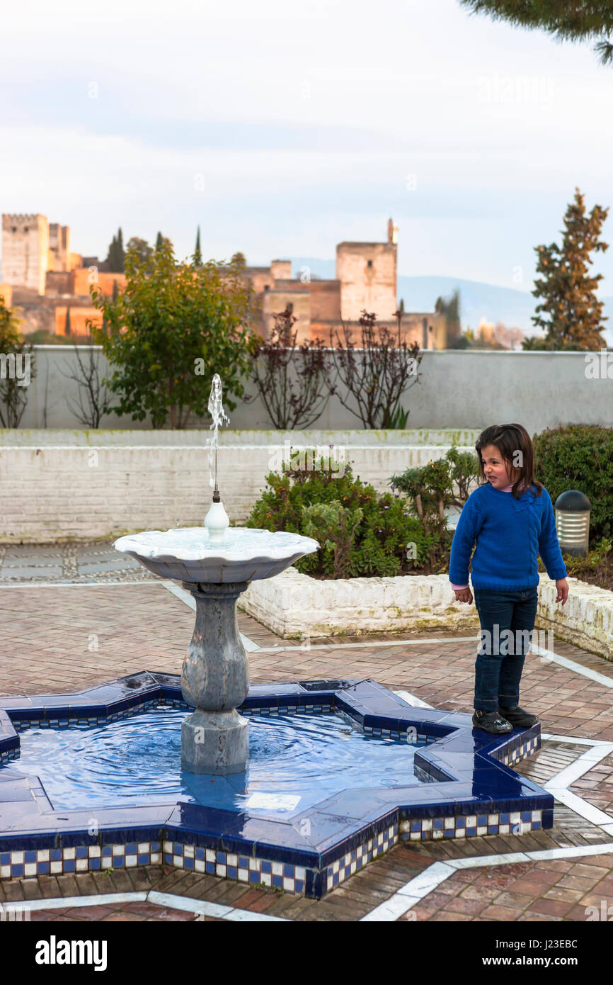 The gardens of the Mezquita Mayor de Granada (The Great Mosque of Granada), with the Alhambra beyond: a child looks at the fountain Stock Photo
