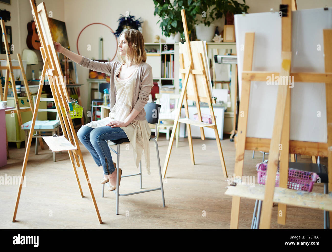 Serious girl sitting in front of easel and drawing Stock Photo - Alamy