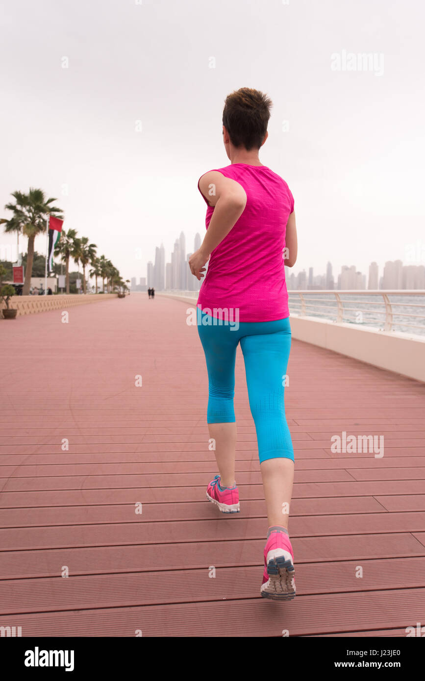 very active young beautiful woman busy running on the promenade along ...