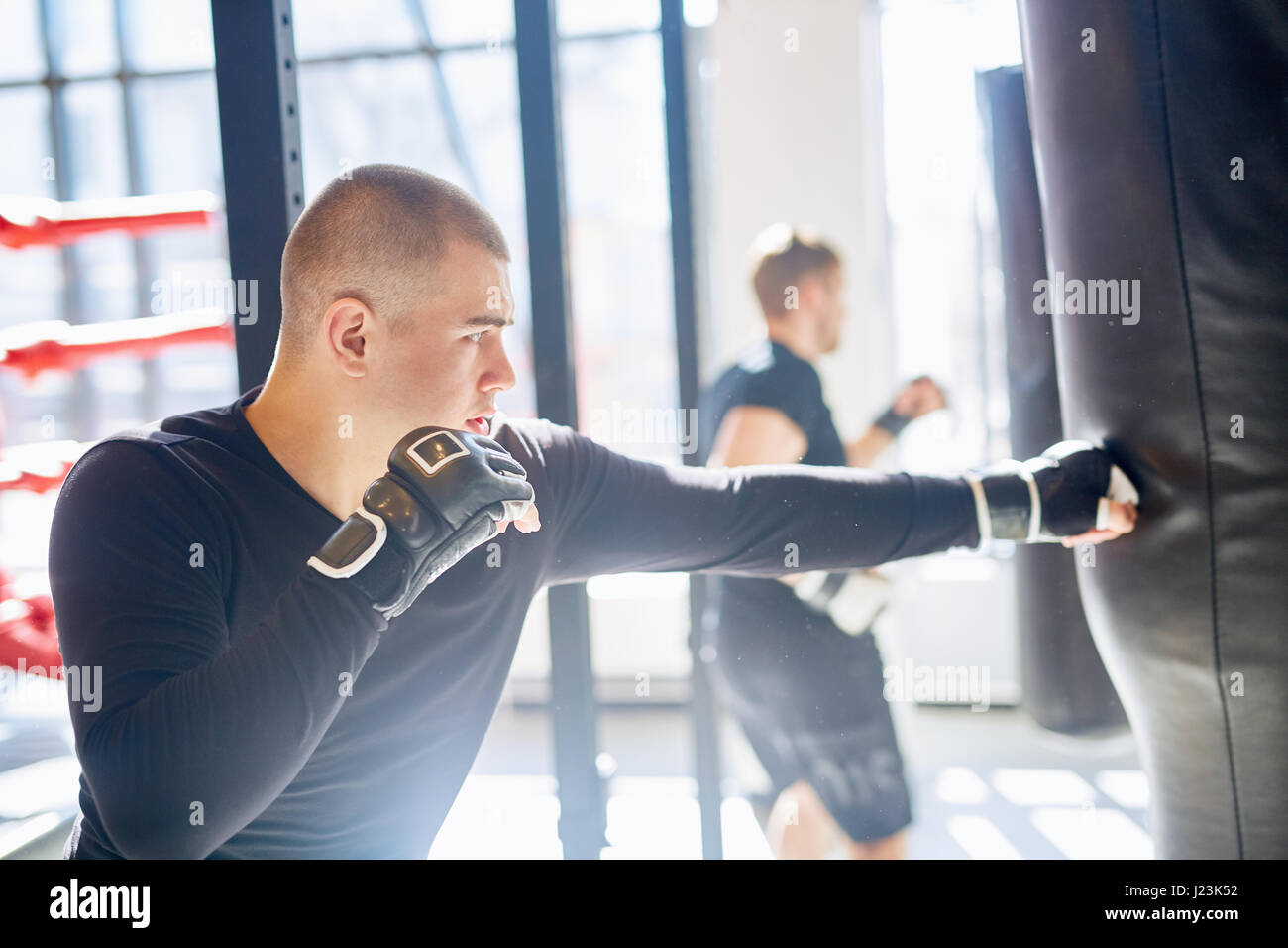 Side view portrait of young muscular boxer hitting punching bag in
