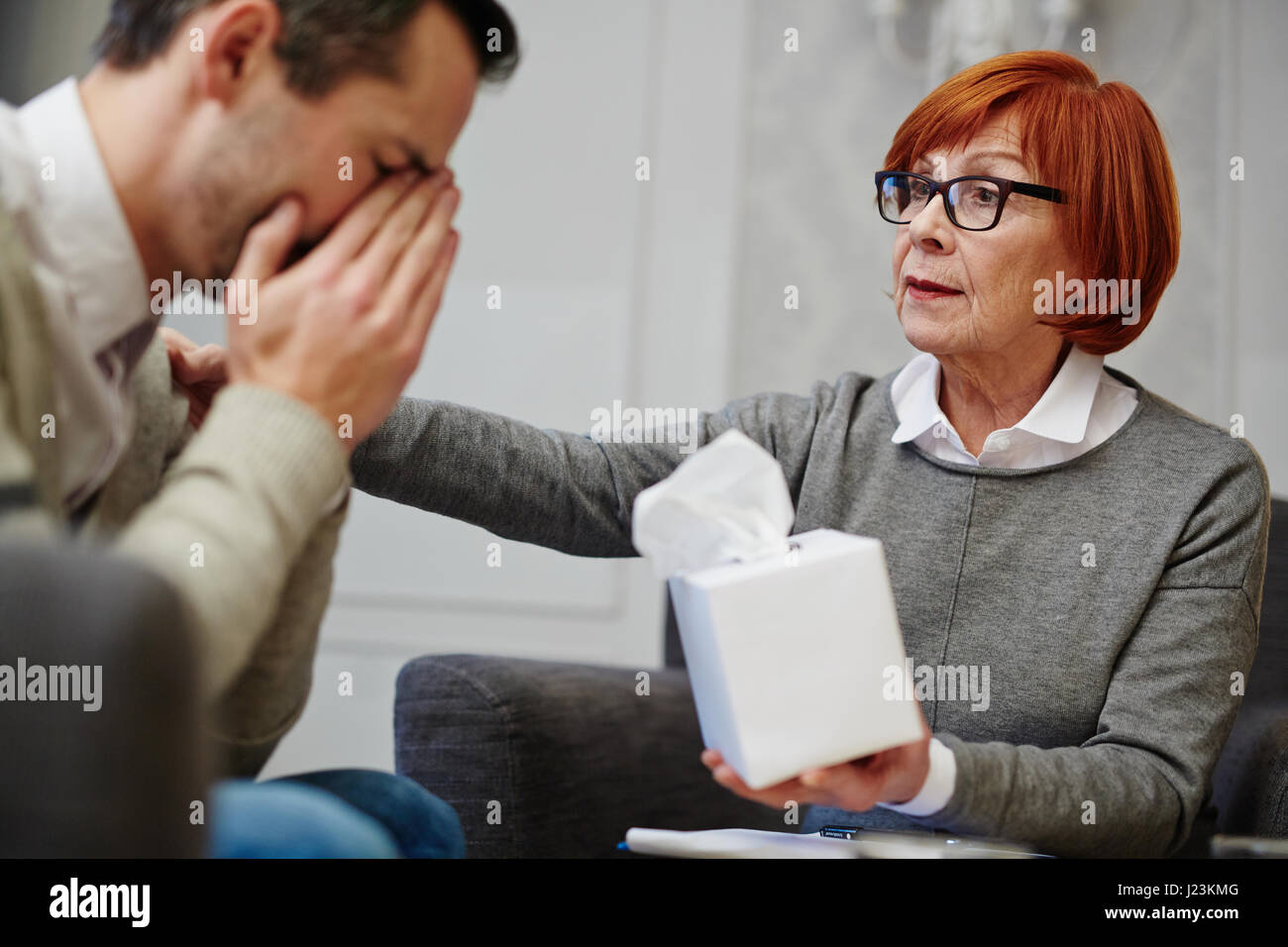 Experienced psychologist comforting patient and giving him box with paper tissues Stock Photo