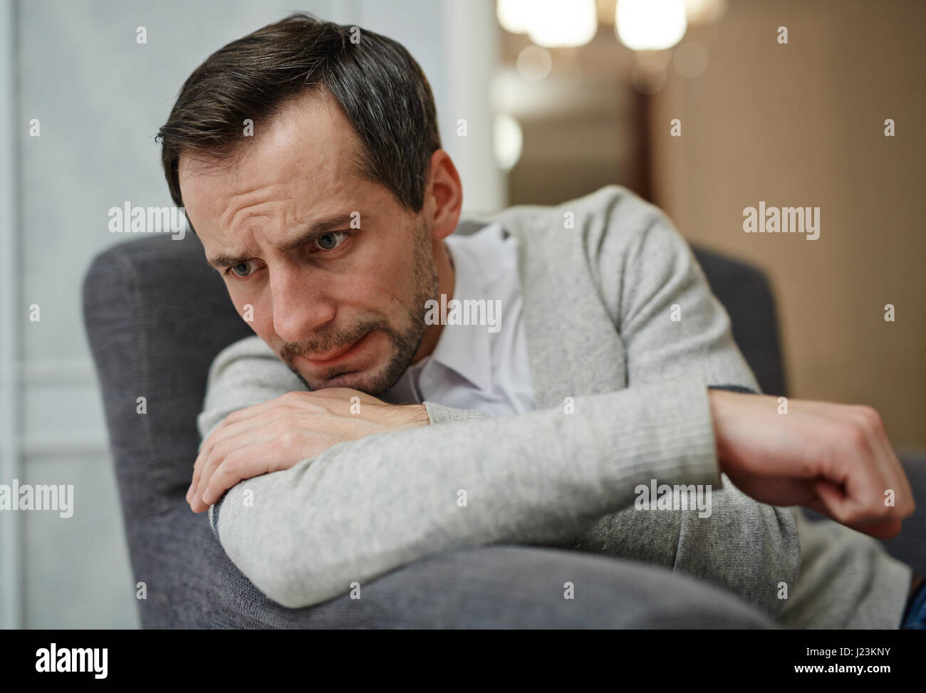 Stressed man sitting in armchair and crying Stock Photo