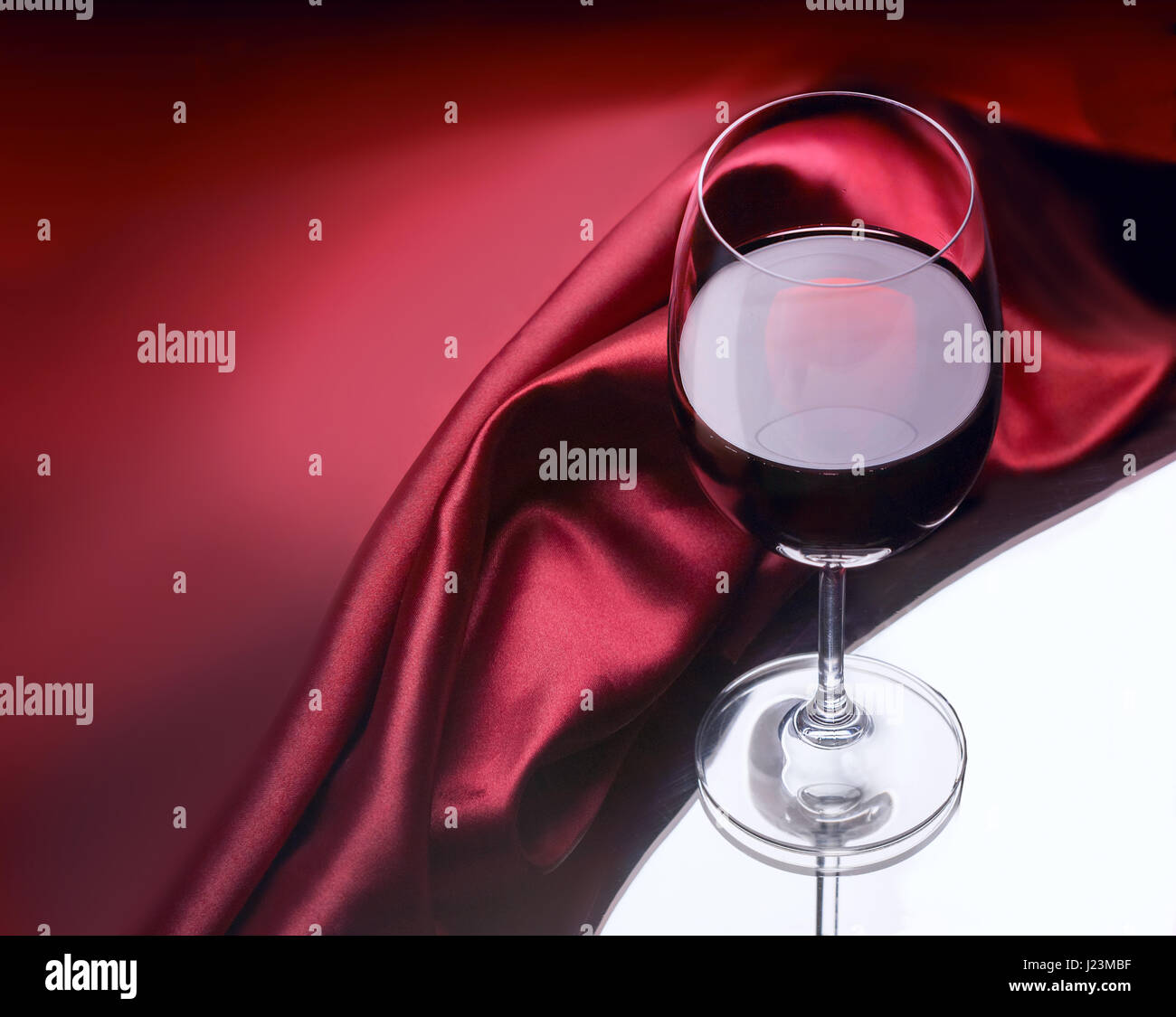 Wineglass of red wine against dark red glossy cloth background Stock Photo