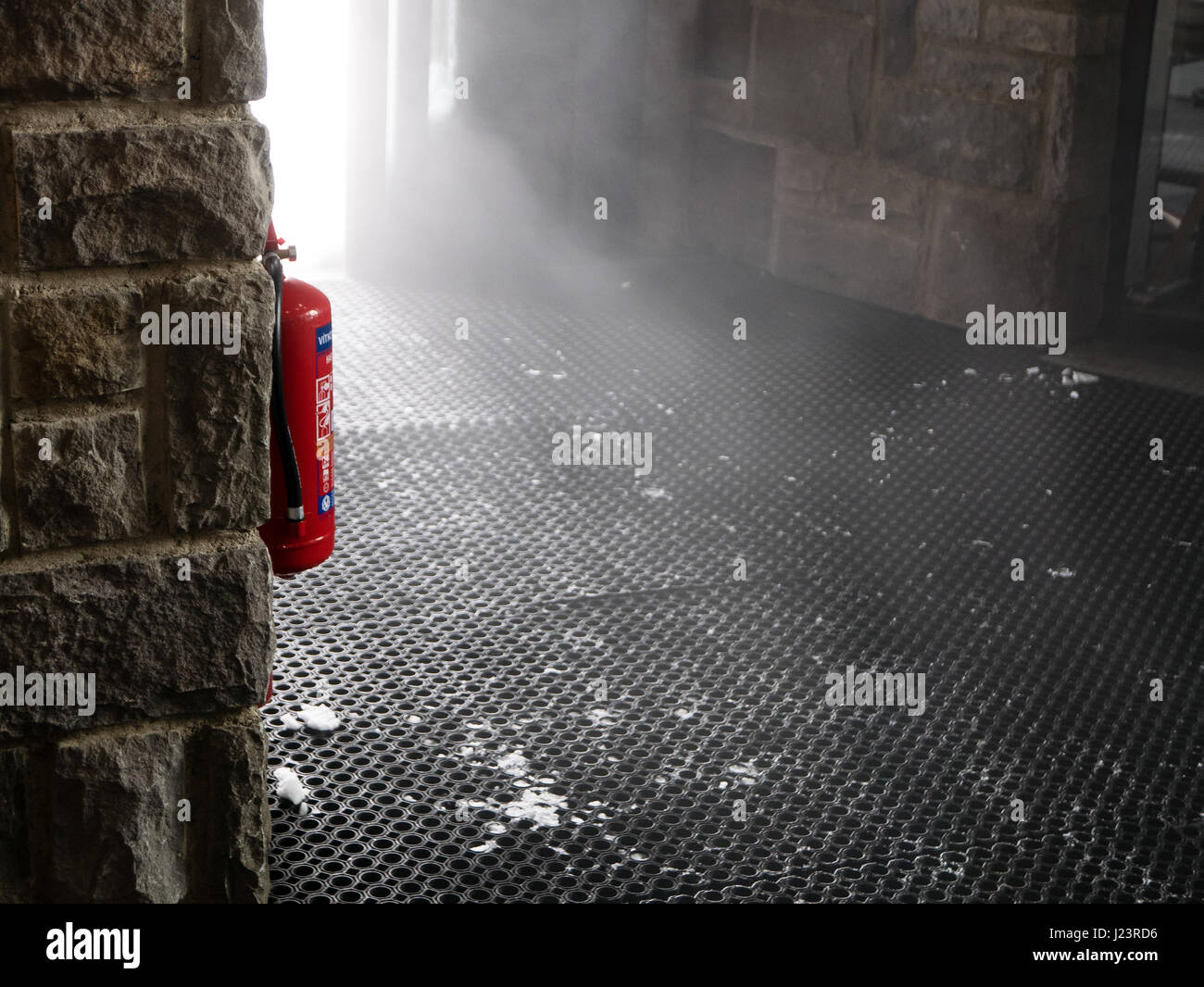 Fire extinguisher hang on the wall, cloud of mist look like smoke, comes through the door. Stock Photo