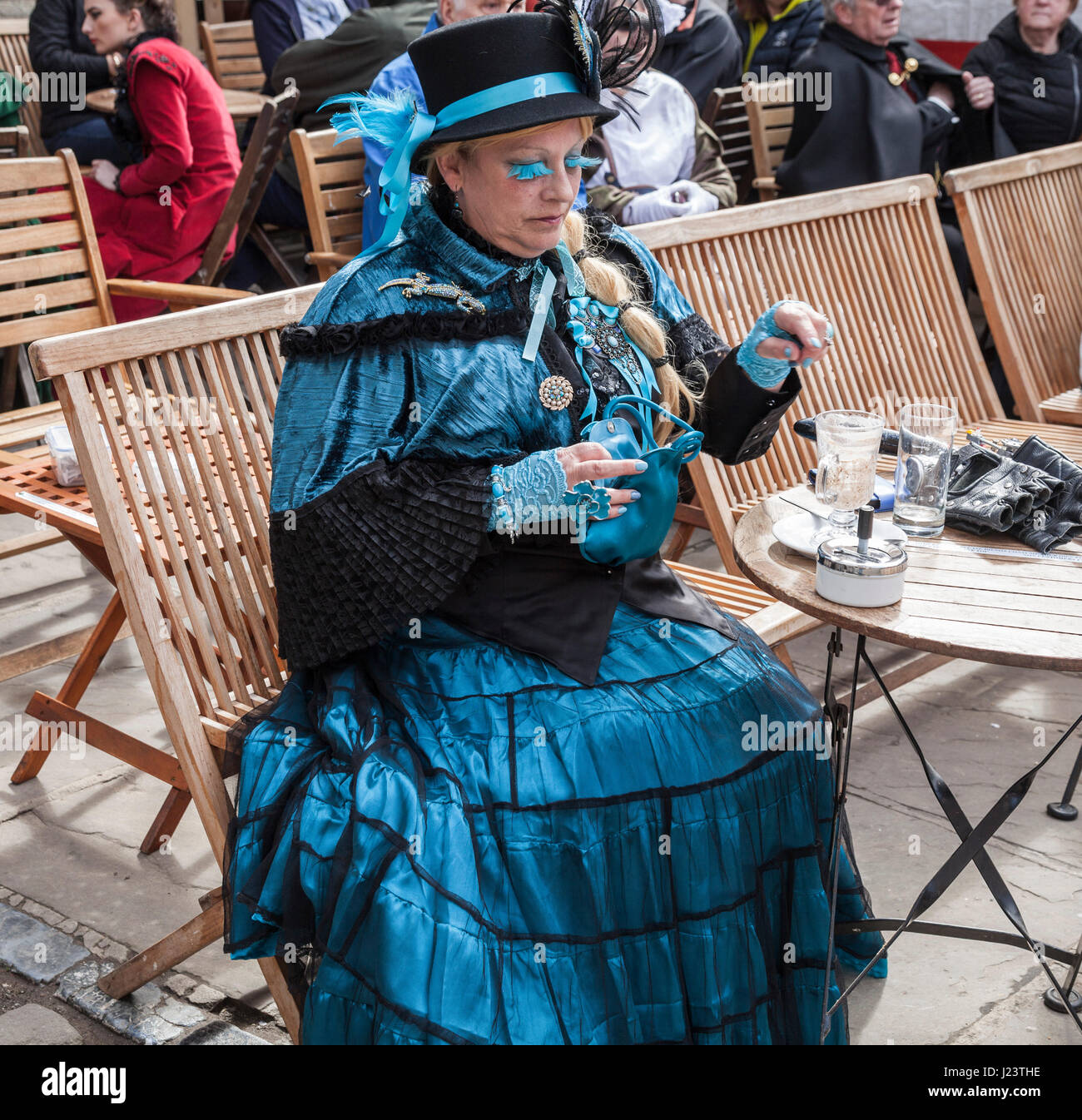 A dressed up woman takes a break from the Whitby goth celebrations and sits down for a drink at a table in the street in North Yorkshire,England. Stock Photo