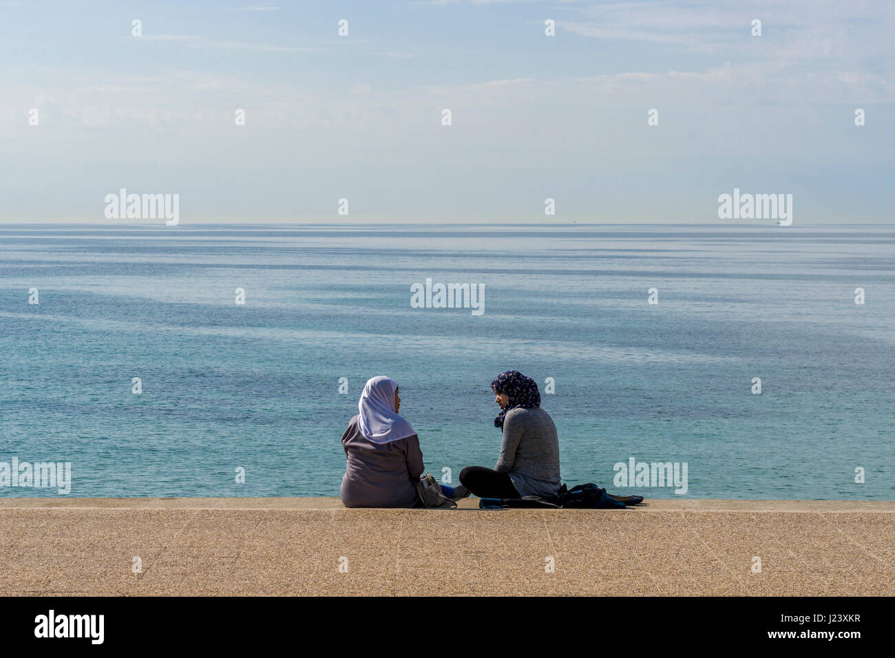 Two muslim women, wearing veil and scarf, are sitting at the mediterranean sea Stock Photo