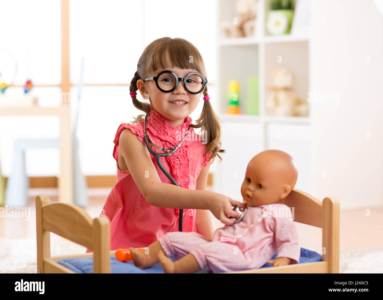 Child in kindergarten. Kid in nursery school. Little girl playing doctor with doll Stock Photo