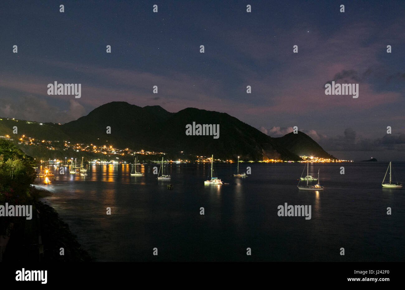 Sailboats illuminate the waters offshore of the town of Roseau, Dominica Stock Photo