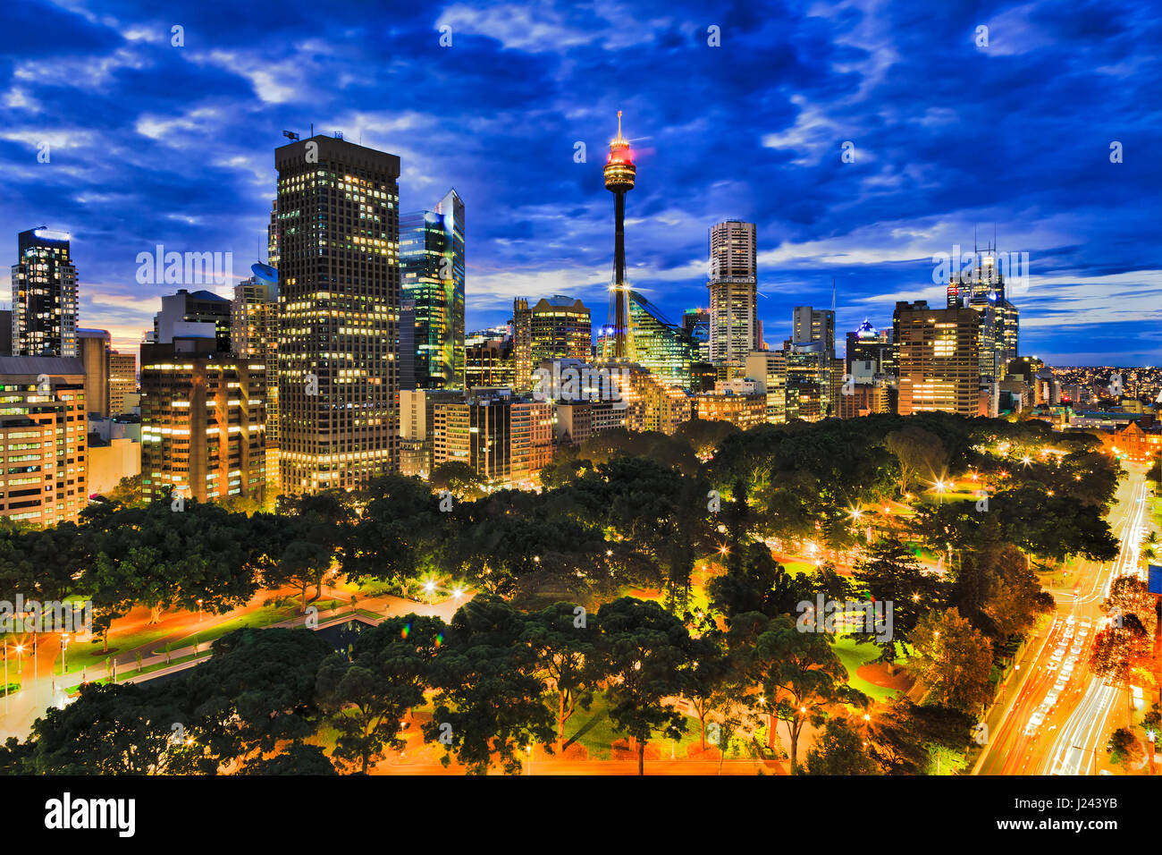 Inside sunset over Sydney city downtown from Hyde park towards high-rises and towers. Brightly illuminated city architecture between traffic roads und Stock Photo