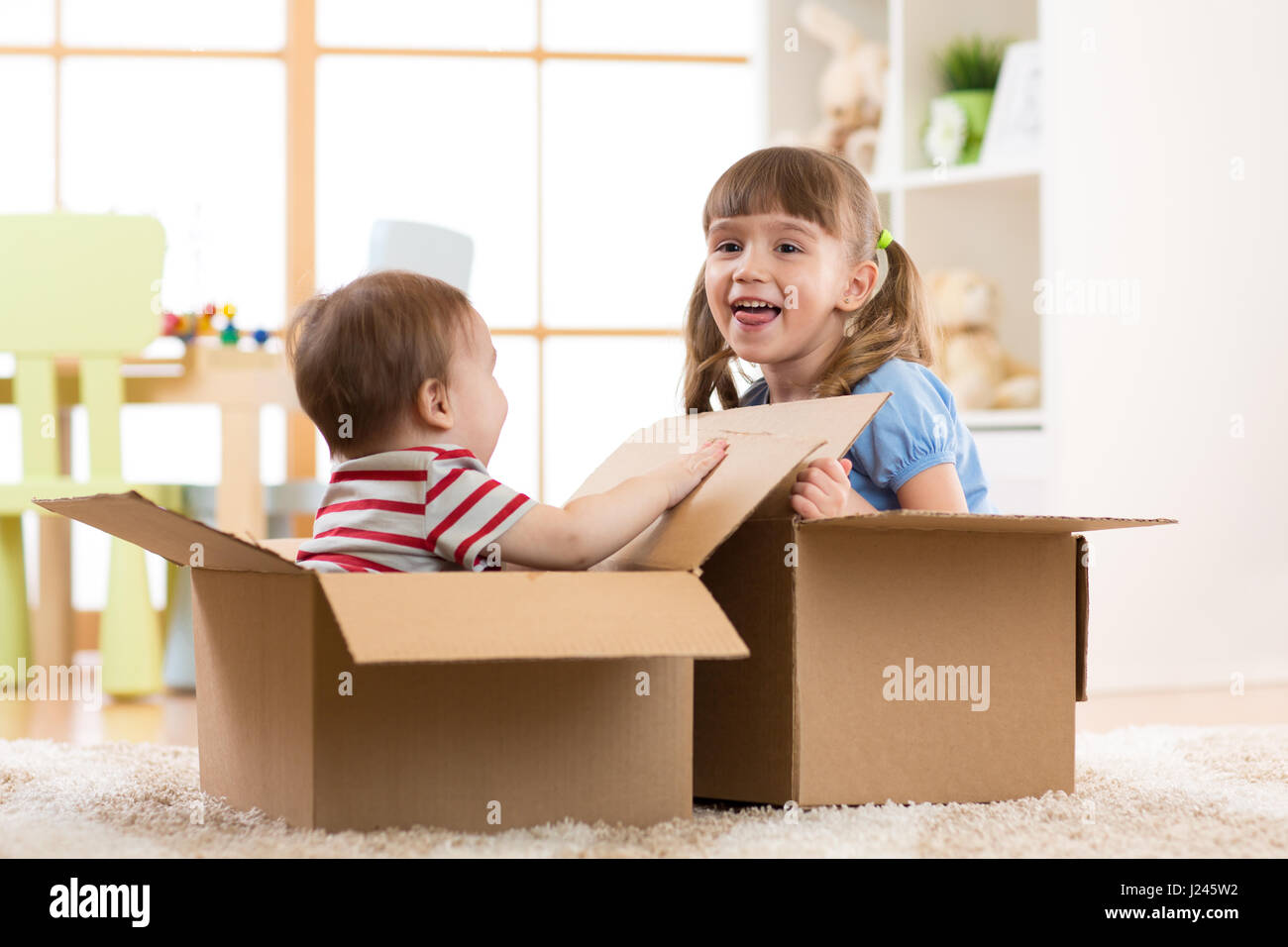 Baby brother and child sister playing in cardboard boxes Stock Photo