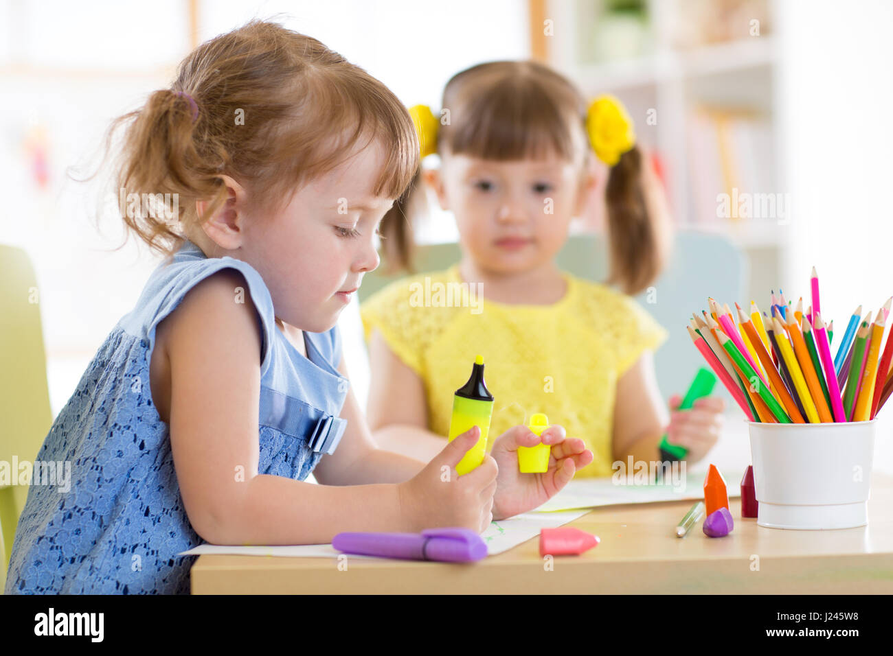 Two beautiful cute kids little girls are drawing at home or daycare centre. Stock Photo