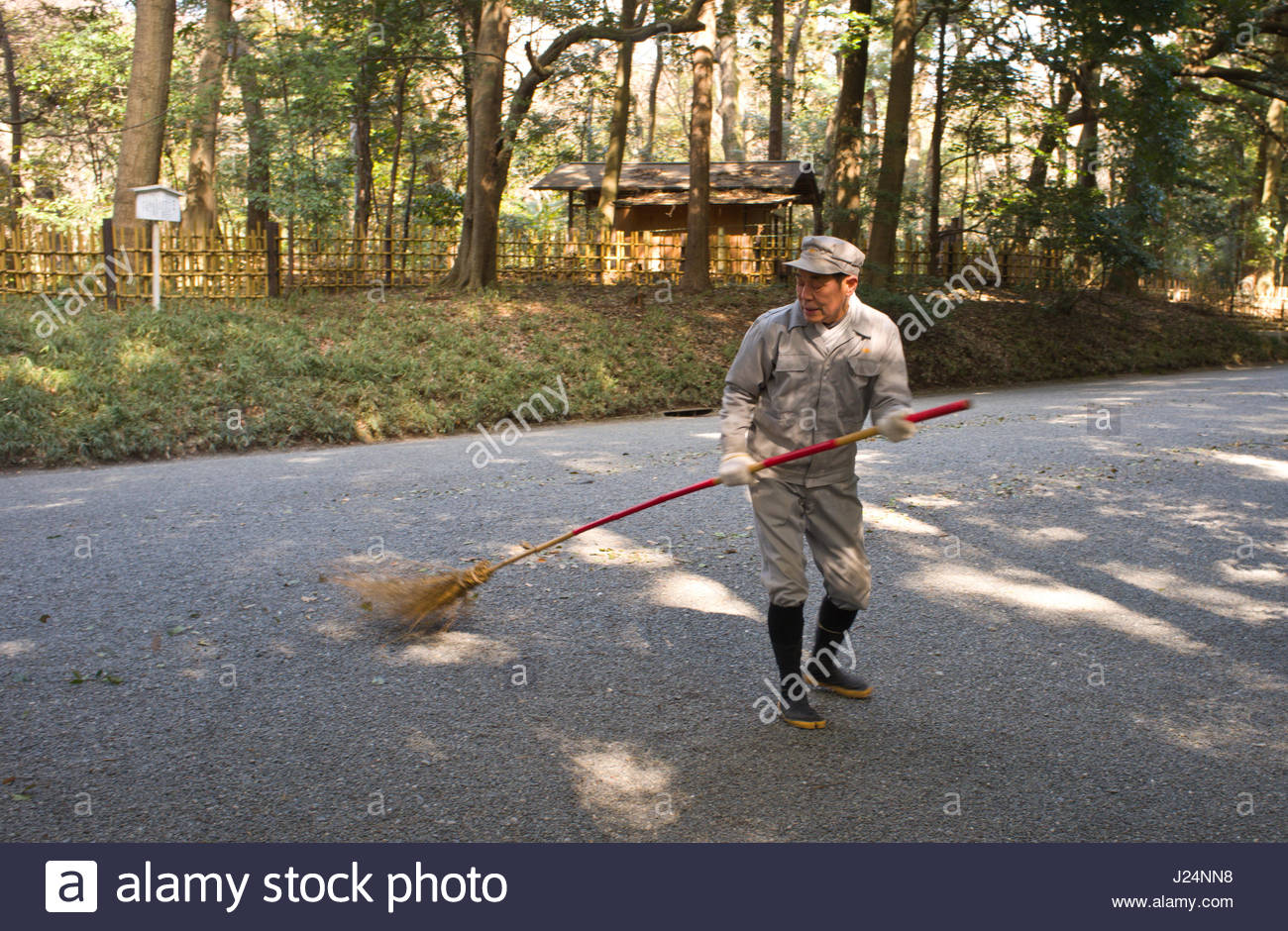 Japanese man using a long handled broom to sweep leaves off the ...