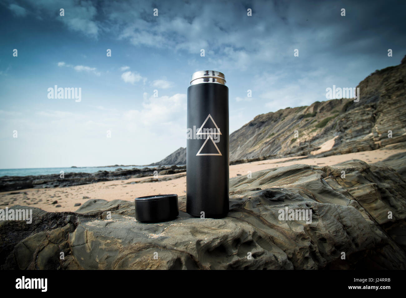Thermos flask sitting on rocks by the sea Stock Photo
