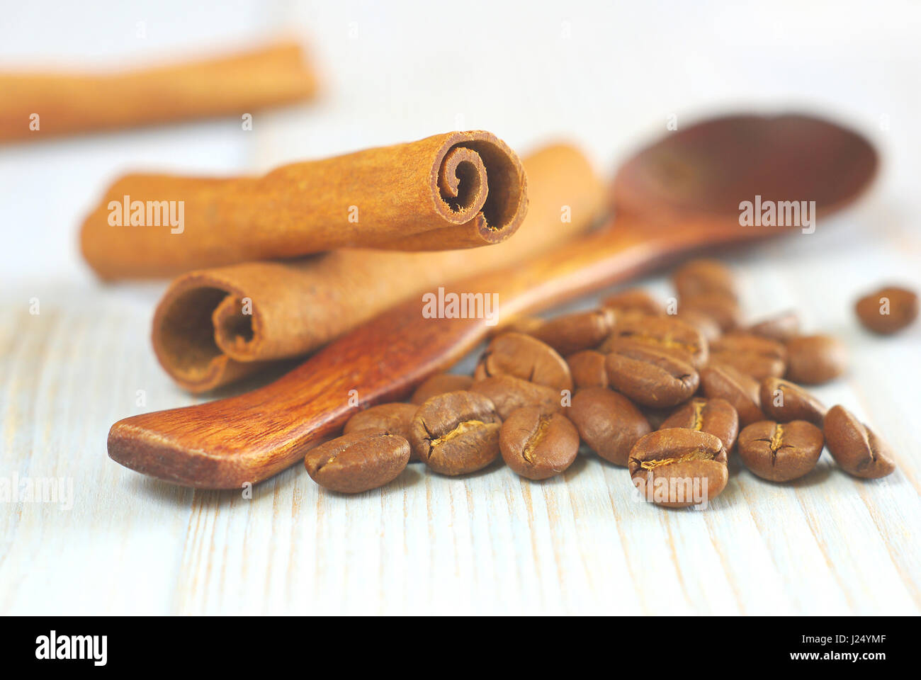 Coffee grains with wooden old-style spoon and cinnamon sticks on vintage table food ingredients background. Selective focus. Coffee aroma drink ingred Stock Photo