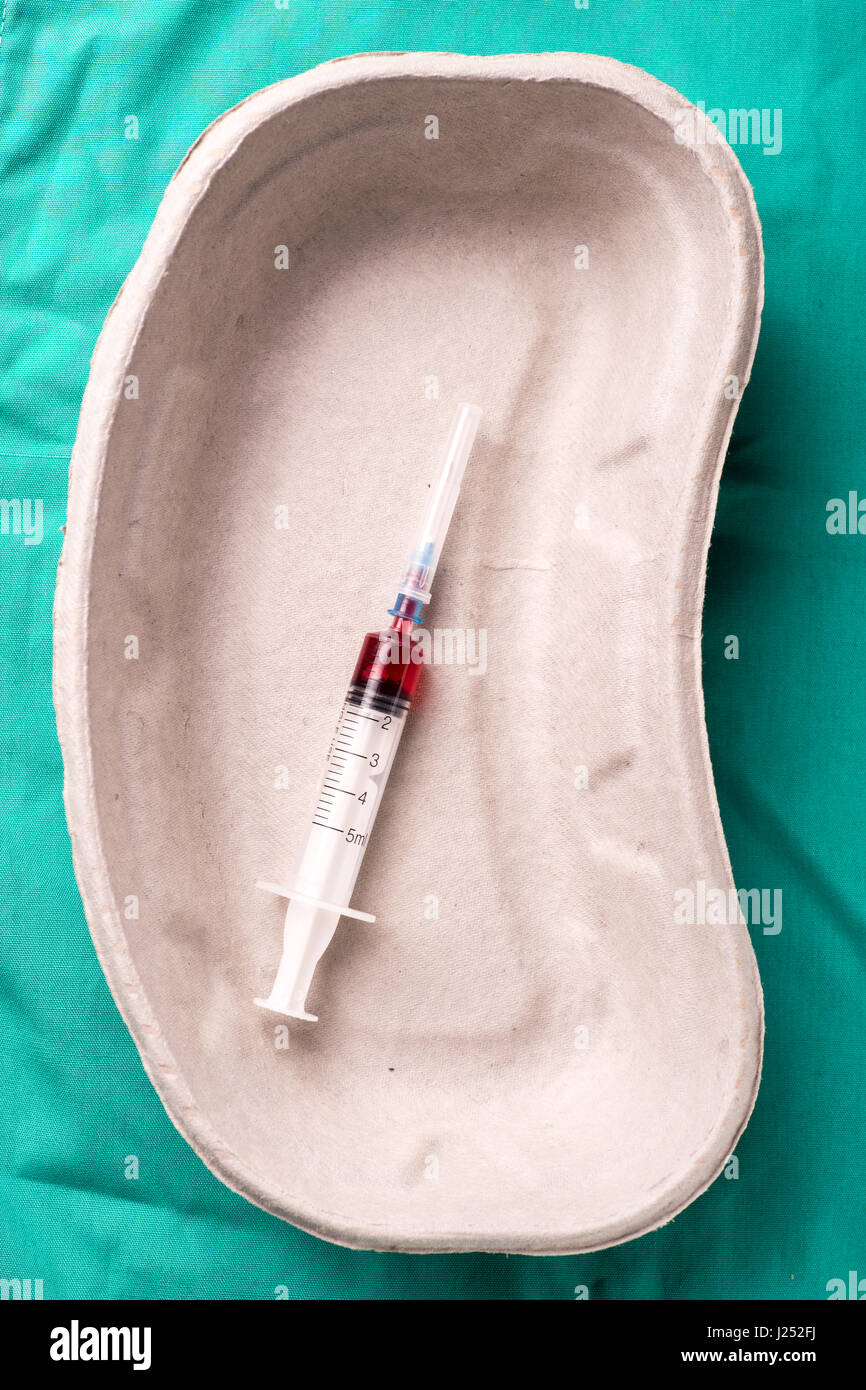 Medical syringe with blood sample lying in a one use capsule on the hospital's green background. The background can be a textile part of a doctor or n Stock Photo