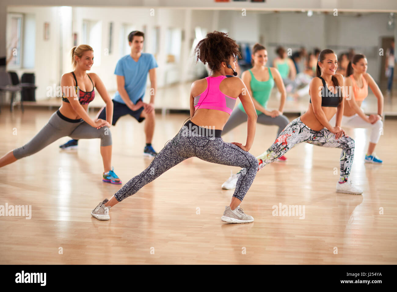 Young group of fitness exercisers in colorful sport clothes with female instructor in fitness class Stock Photo