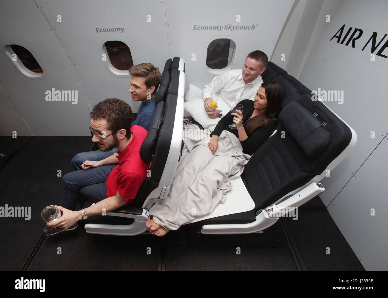Air New Zealand staff Chris Allison and Nishi Prasad (right) demonstrate the Economy Skycouch flexible seating in a mock-up aircraft cabin, during the launch of Air New Zealand's pop-up event 'This is How We Fly', which showcases the airline's on-board facilities, in Soho, London. Stock Photo