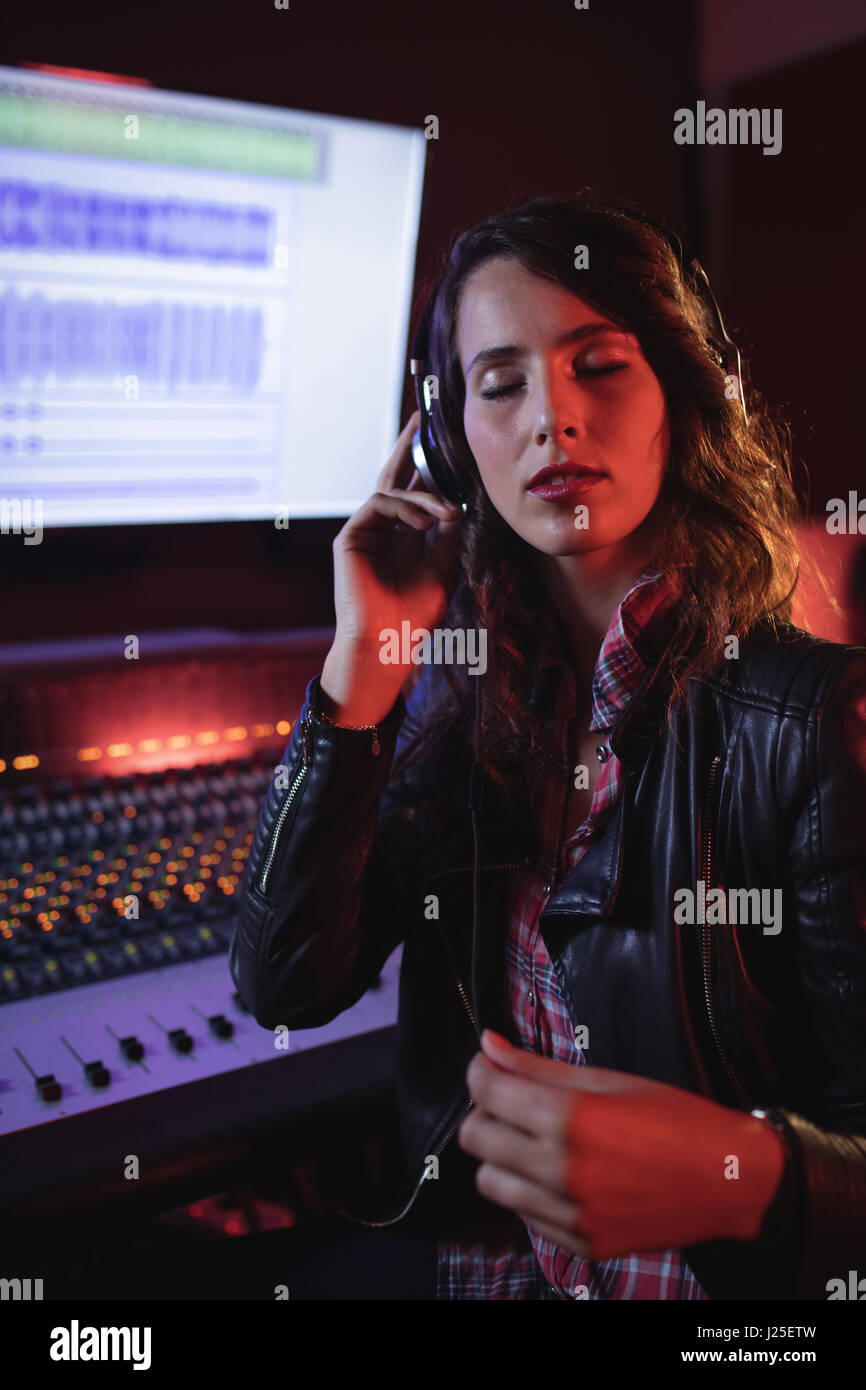 Female audio engineer listening music on headphones in recording studio