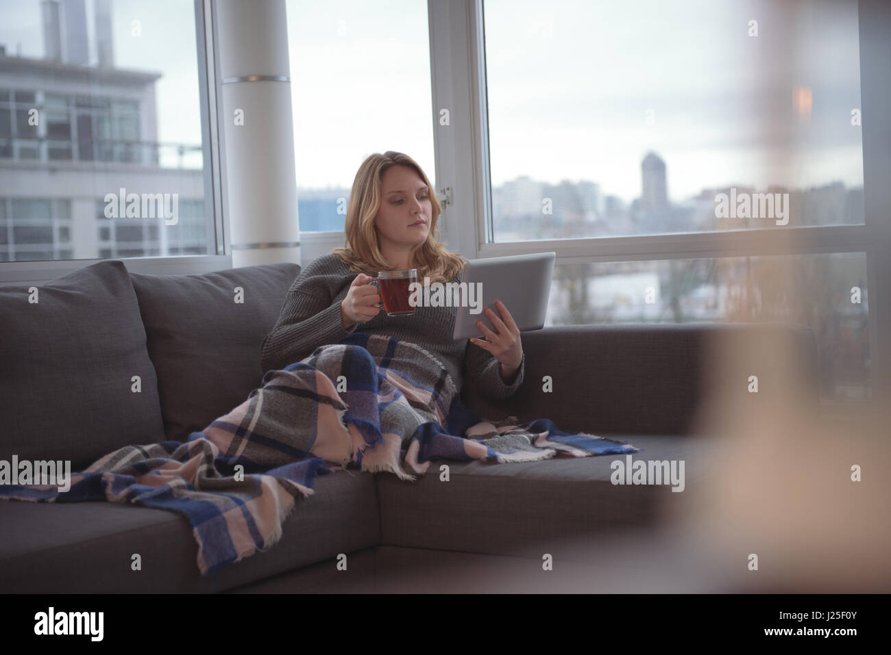 Woman using digital tablet while having coffee on sofa at home Stock ...