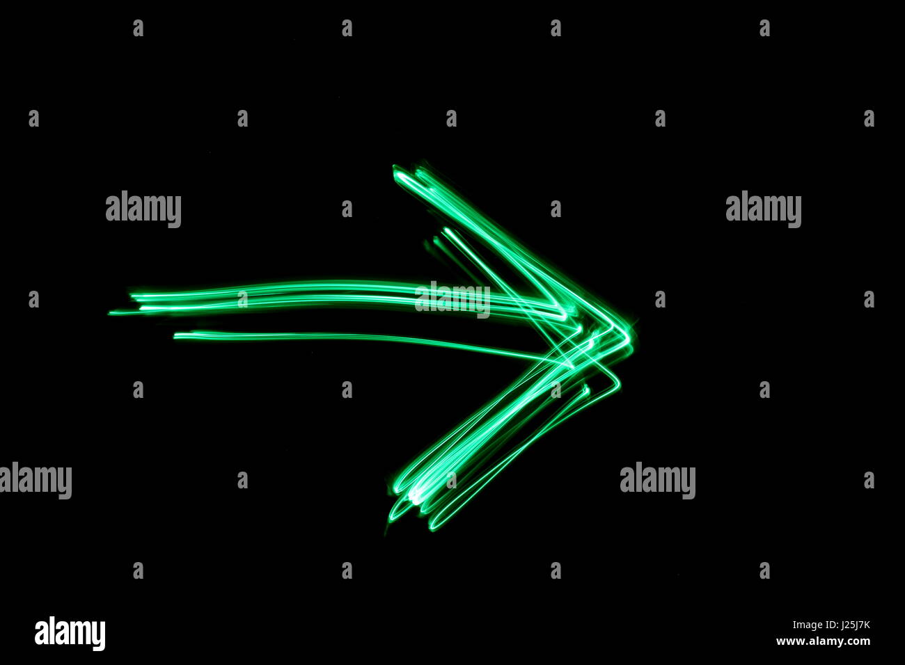 Long exposure photograph of neon green colour in an abstract arrow outline against a black background. Light painting photography, abstract colour Stock Photo