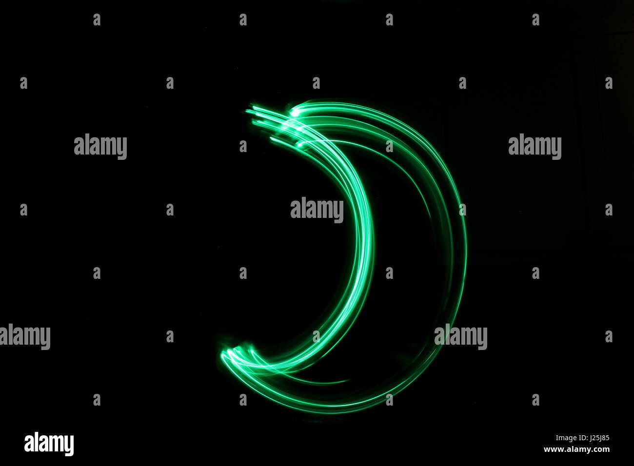 Long exposure photograph of neon green colour in an abstract moon shape against a black background. Light painting photography, abstract colour Stock Photo