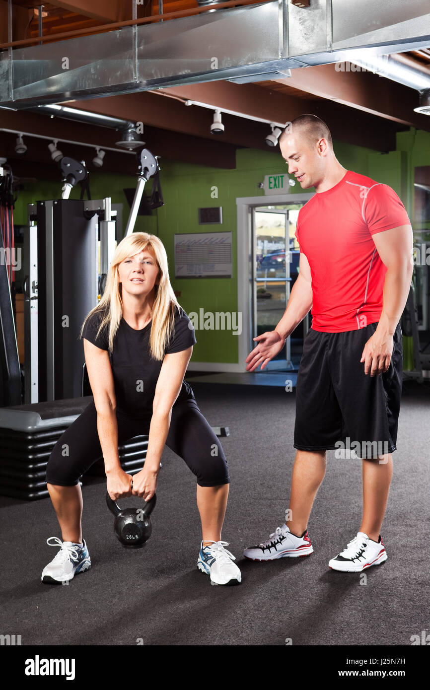 A shot of a male personal trainer assisting a woman lifting weights ...