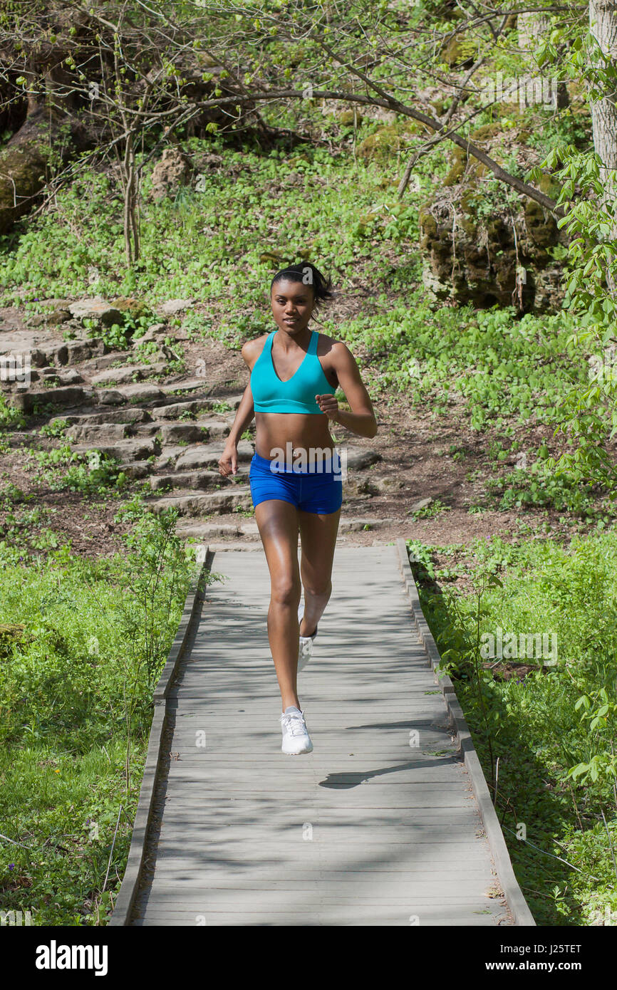 Fit pretty black girl in sports bra and shorts running down a