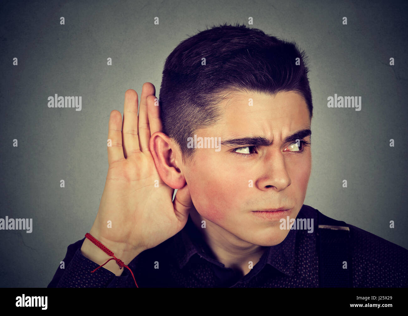 Curious worried man with hand to ear carefully secretly listening to gossip conversation isolated on gray background Stock Photo