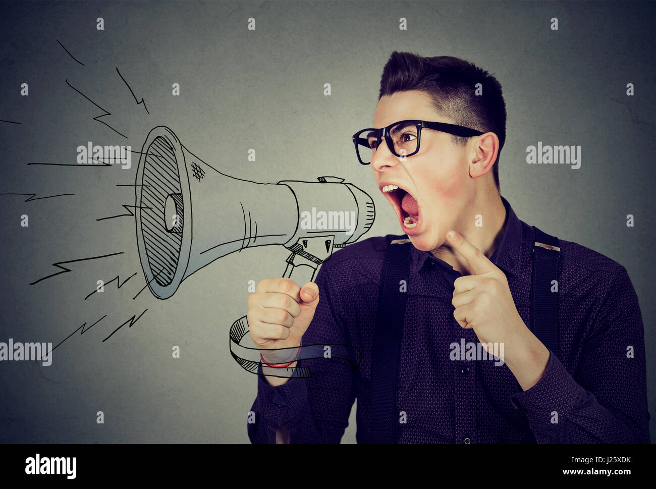 Angry young man screaming in megaphone isolated on gray background. Negative face expression emotion feeling. Propaganda, breaking news, power of soci Stock Photo