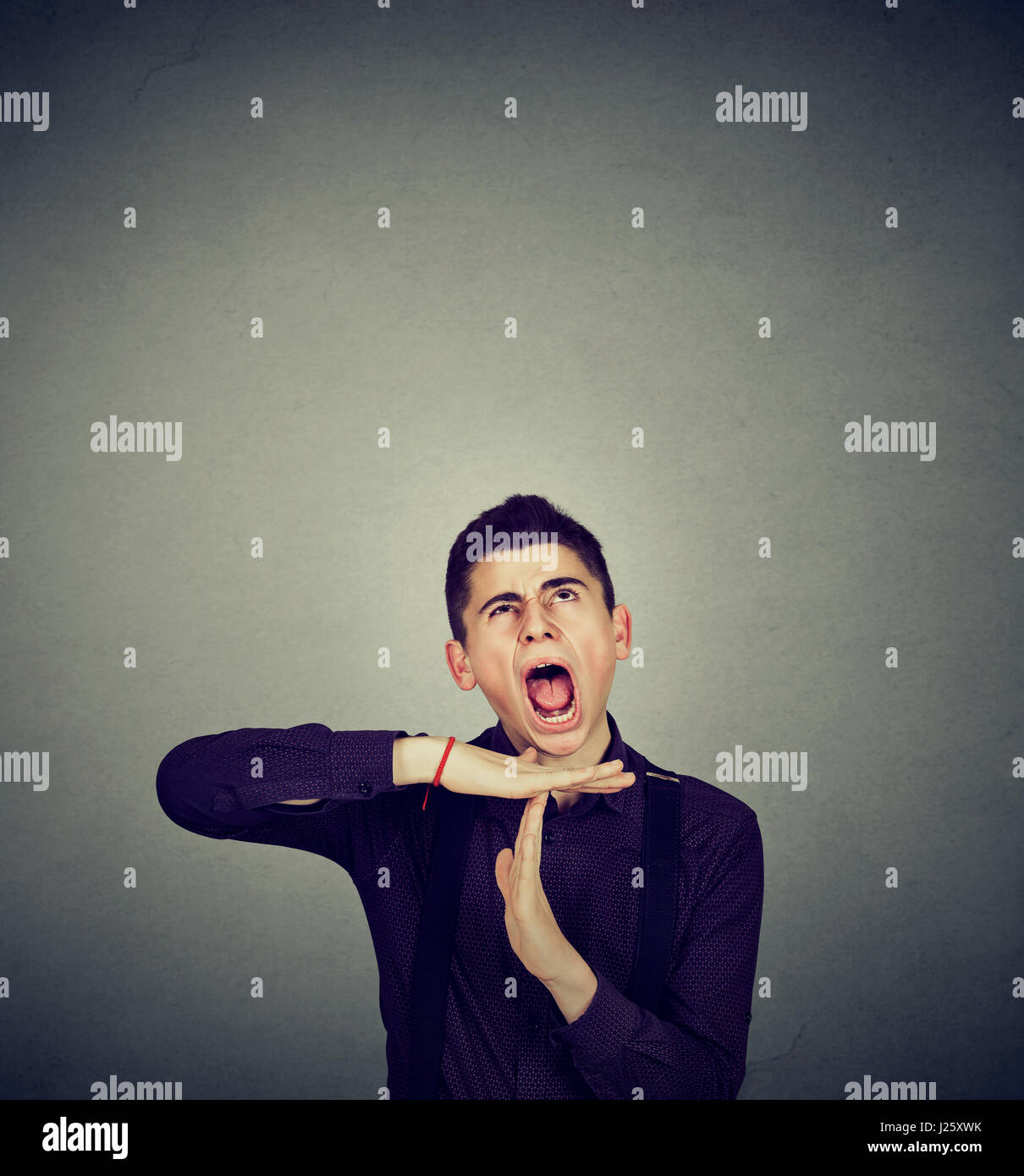 Overwhelmed man showing time out hand gesture, frustrated screaming to stop isolated on grey wall background. Too many things to do concept Stock Photo