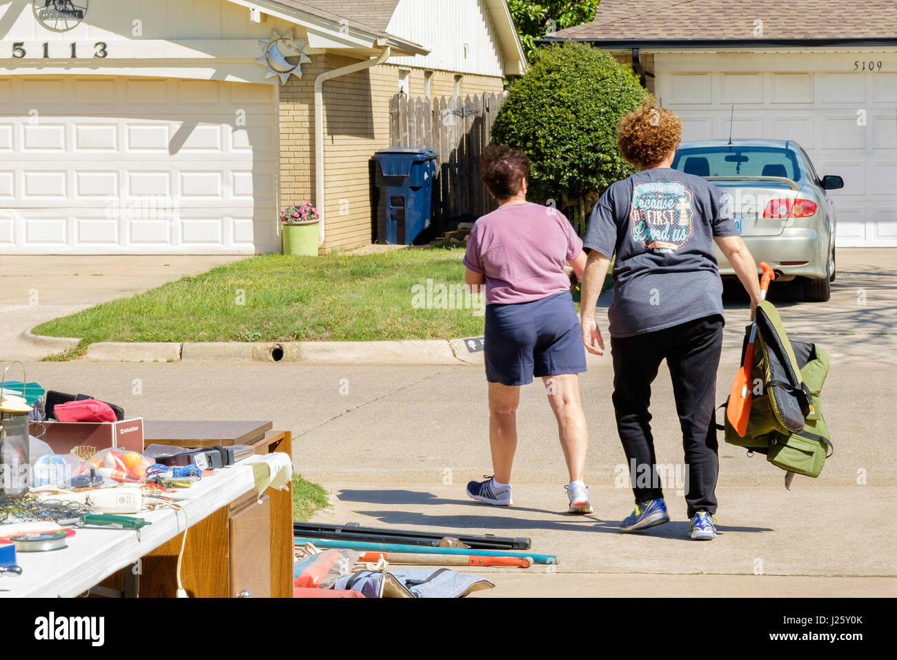 Two mature women walk away after purchasing merchandise including life jackets at a garage sale, or rummage sale, in Oklahoma City, Oklahoma, USA. Stock Photo