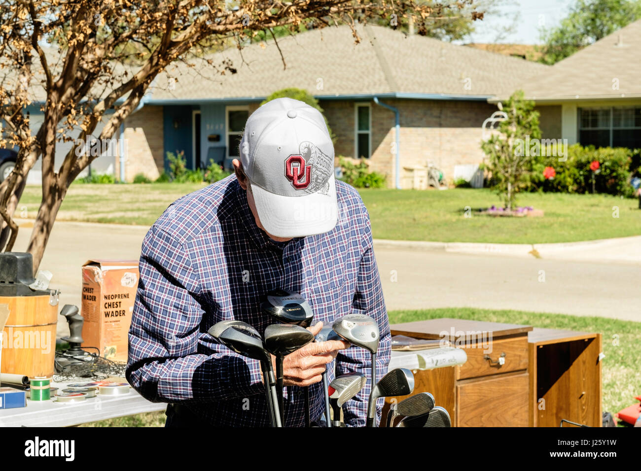 An Elderly Caucasian Man Looks At Golf Clubs At A Garage Sale In