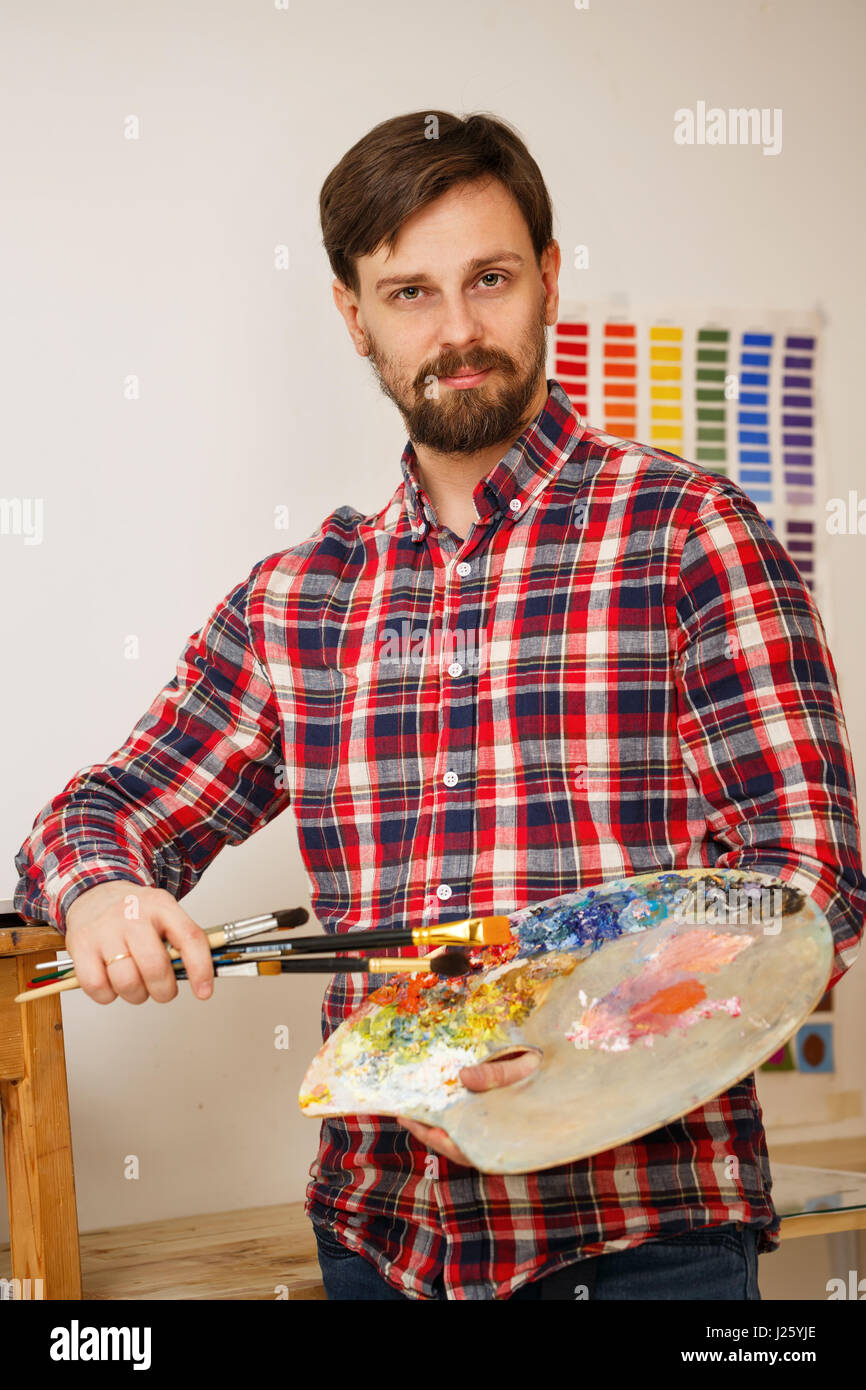 Man Using Art Tools Man artist holds in his hands a paintbrush and a wooden palette with ...