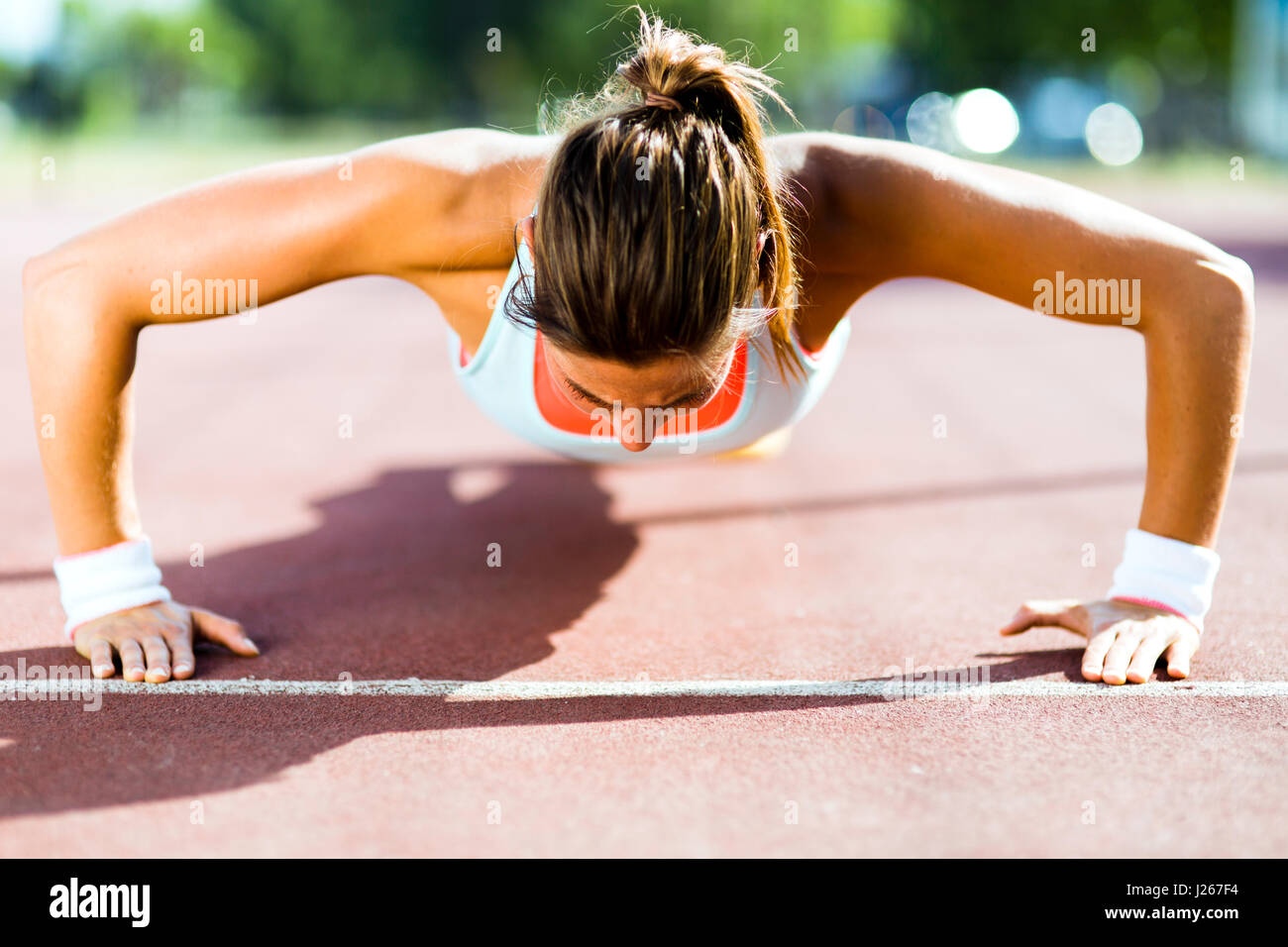Focused young beautiful woman doing push-ups outdoors on a hot summer day Stock Photo