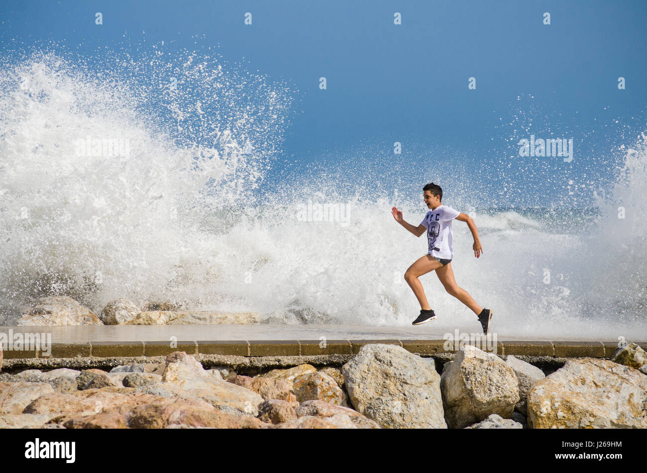 Excited boy on pier running away from splashing water on pier, young boy, teenage, teenager, Spain. Stock Photo