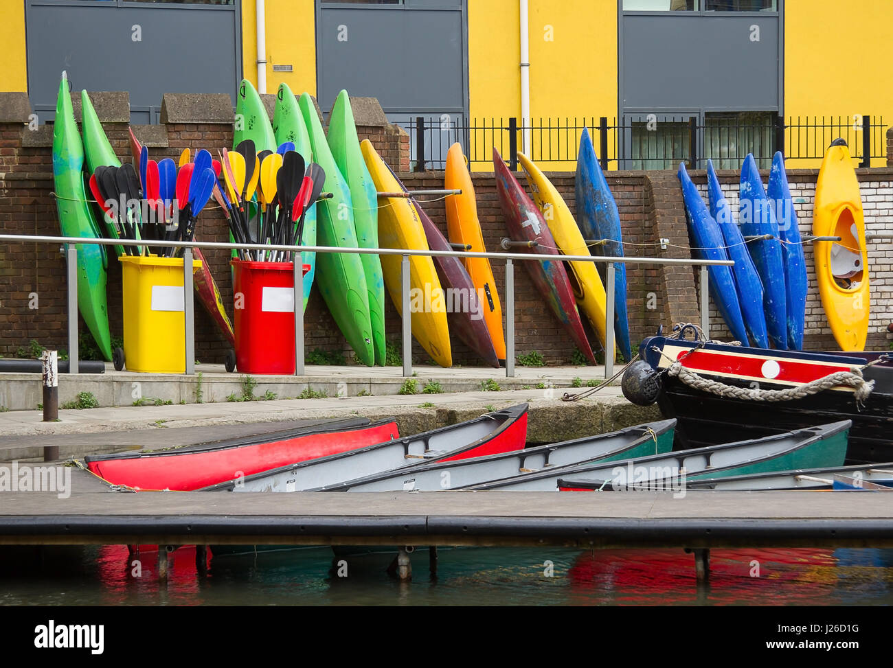 photo of a group of different colored canoes standing up on one end in a row Stock Photo