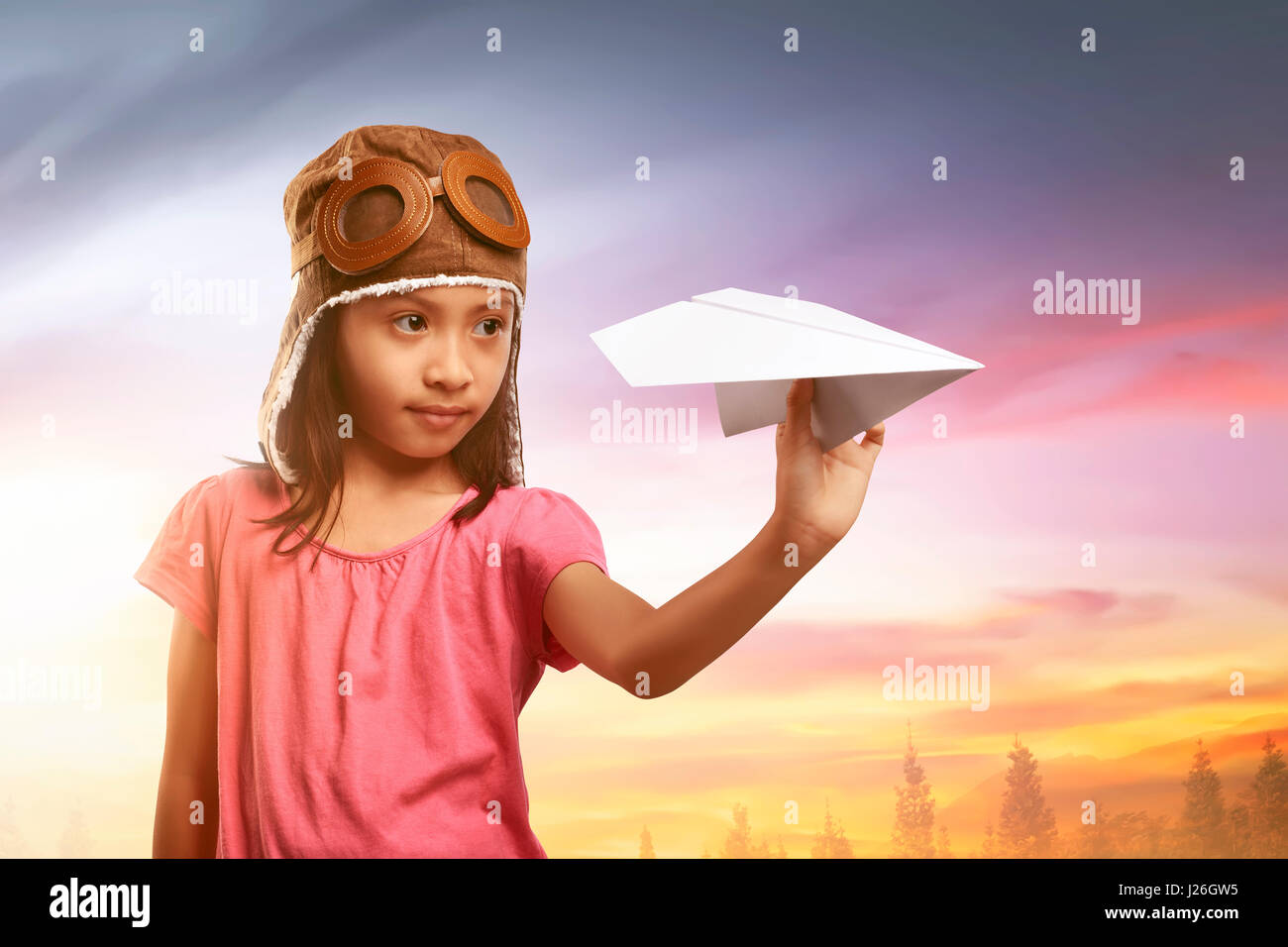 Happy asian child in aviator helmet playing with paper planes on the field Stock Photo
