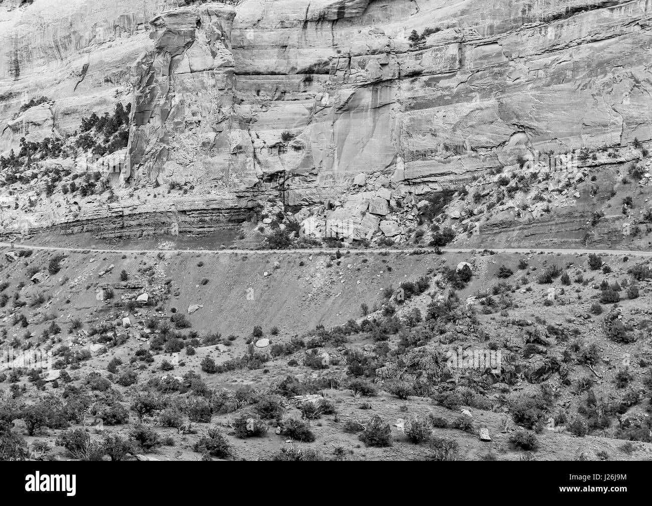 Part of the Rim Rock Drive, the road going through the Colorado National Monument, in front of a cliff. The picture is in monochrome. Stock Photo