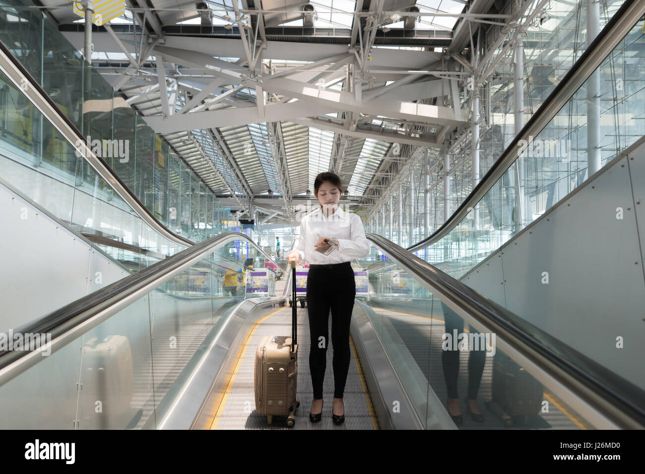 Asian young businesswoman with luggage down the escalator in airport. business travel. Stock Photo