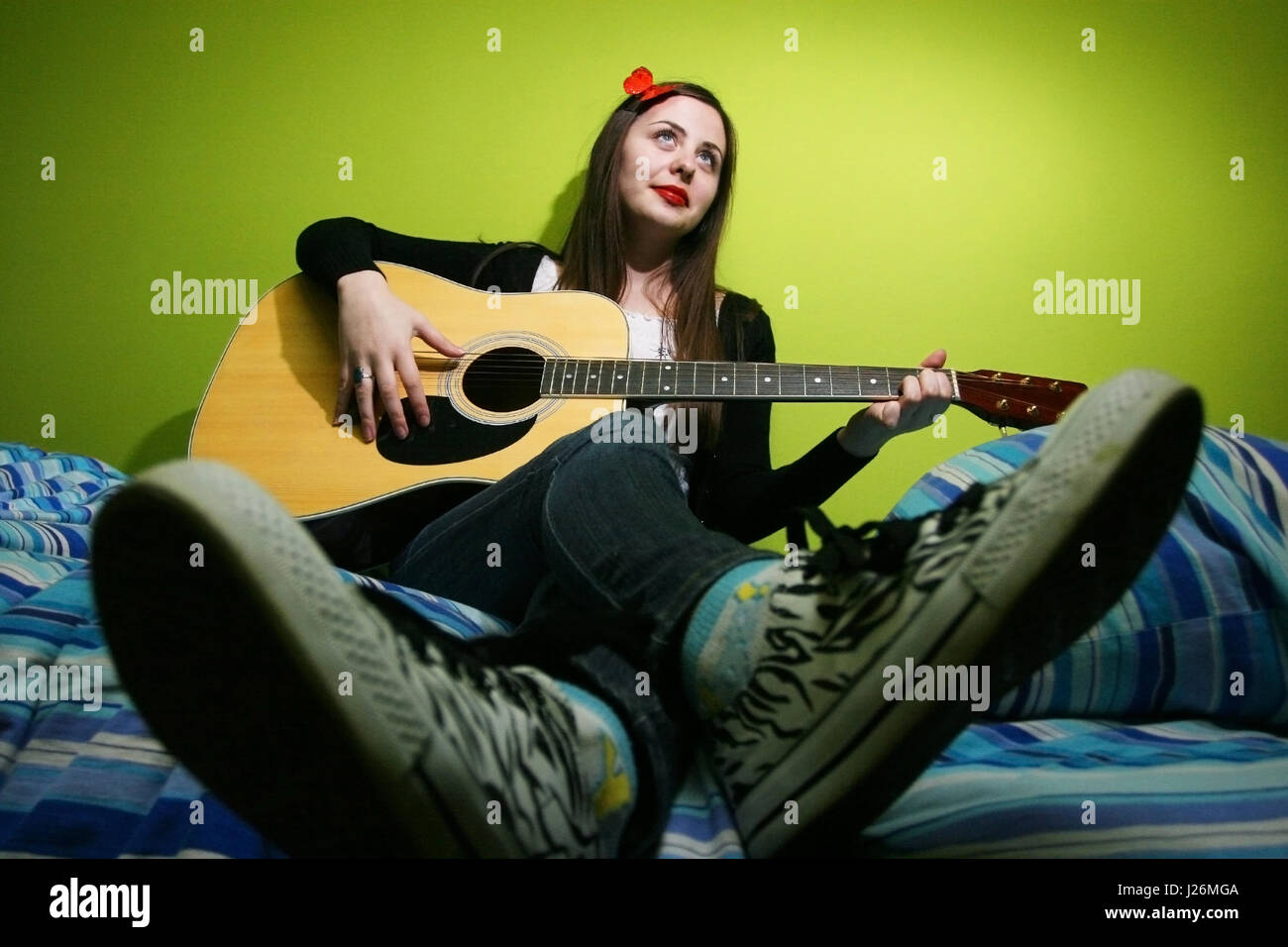 Young brunette playing the guitar on bed. Stock Photo