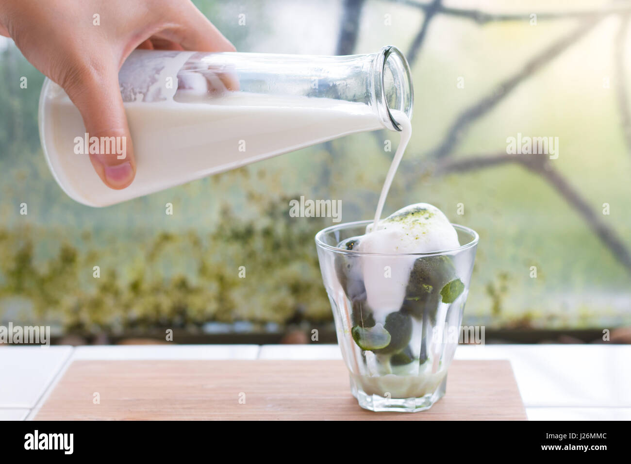 Ice green tea with pouring milk in the glass on the background of nature. Stock Photo