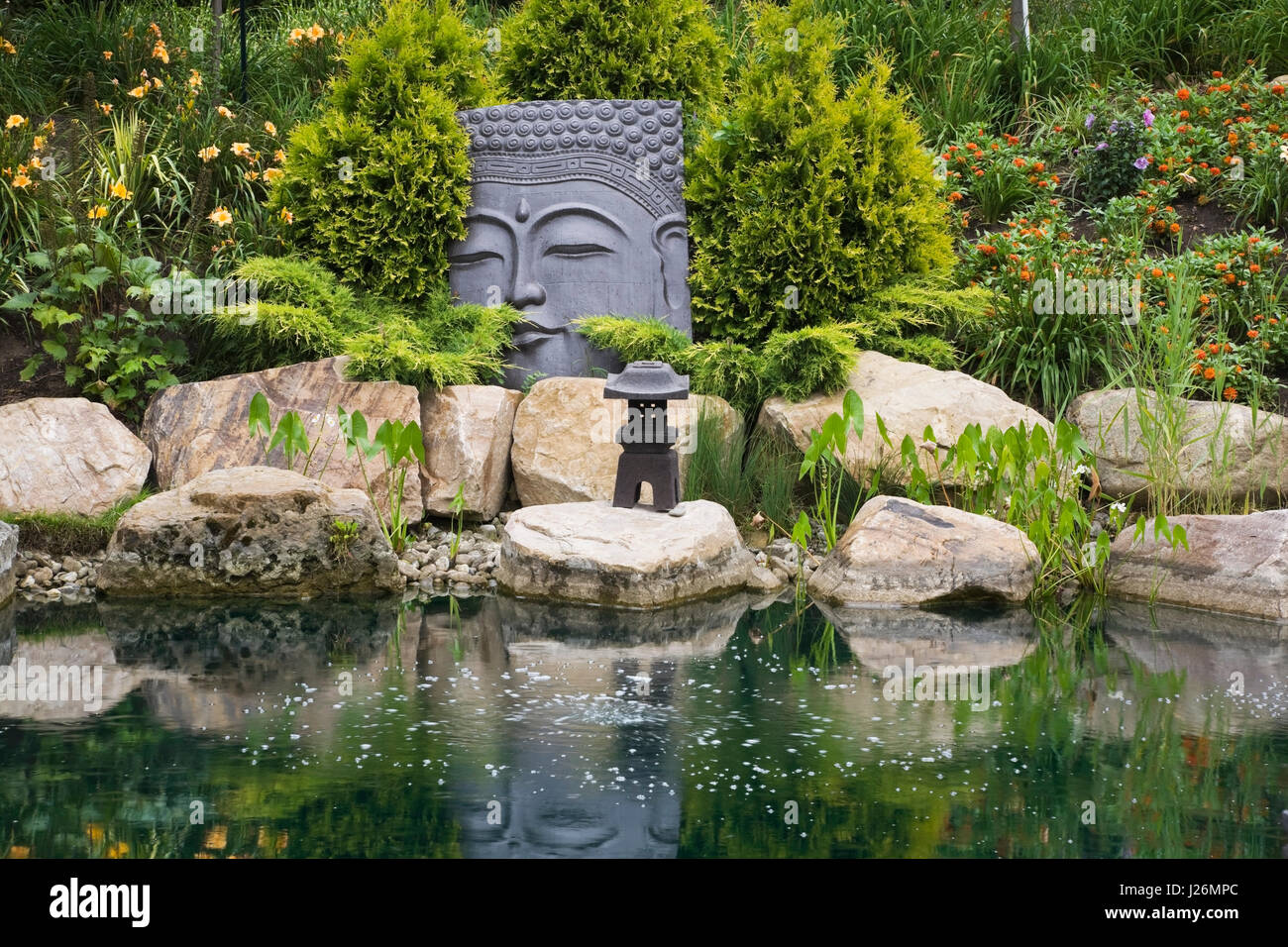 Pond with large sculptured head in the Zen garden at the Route des Gerbes d'Angelica garden in summer, Mirabel, Laurentians, Quebec, Canada Stock Photo