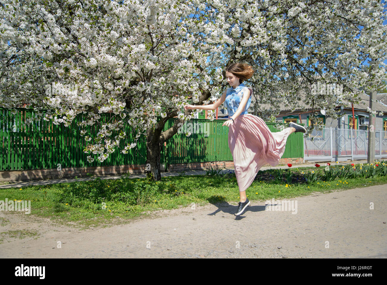 A young girl runs, bouncing against the background of a blossoming cherry tree Stock Photo
