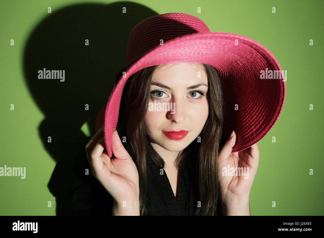 Portrait of a young woman with pink straw hat looking at the camera on ...