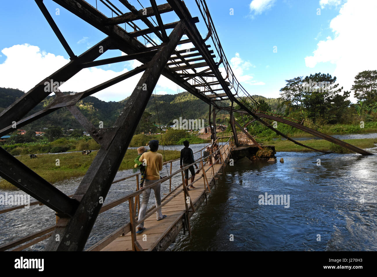 Pedestrians walking over a wooden bridge  in Ranomafana town that replaced the iron one  above it which was  destroyed in a cyclone. Stock Photo