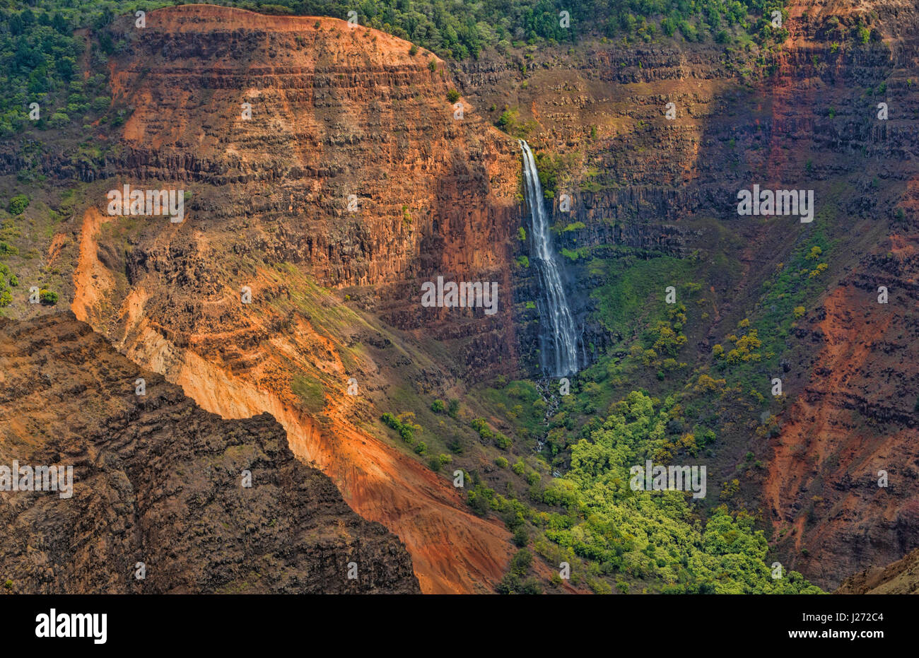 Kauai Hawaii scenic Waimea Canyon State Park red cliffs from above canyon with distant waterfall Stock Photo