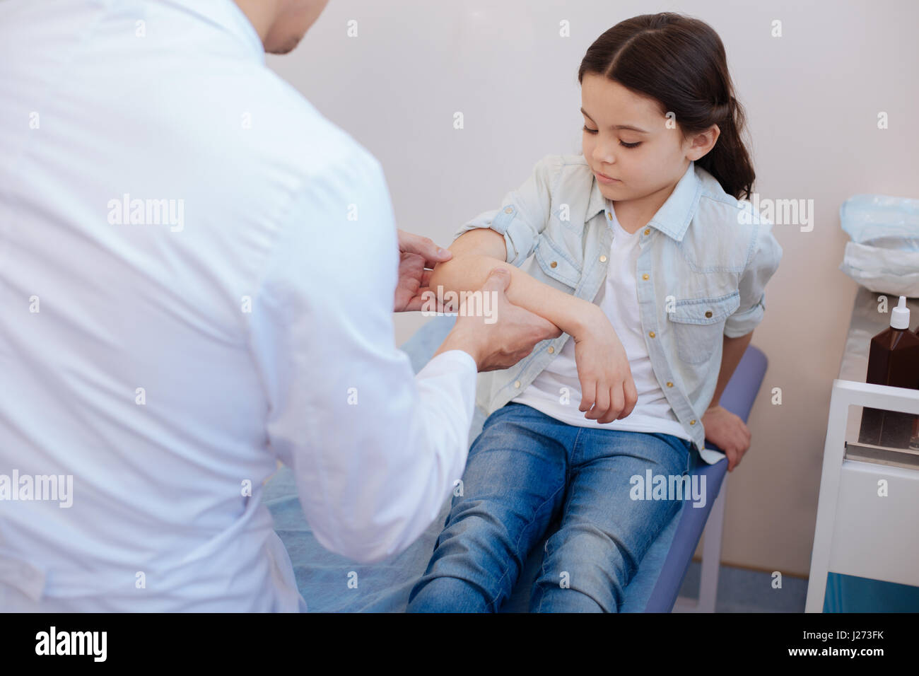 Visit to a rheumatologist. Nice cute serious girl holding her arm up and being examined by a rheumatologist while visiting a hospital Stock Photo