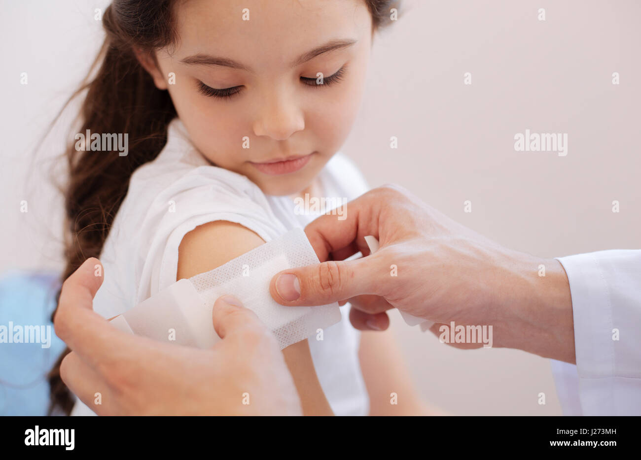 Shoulder injury. Nice professional male doctor holding a plaster and putting it on the girls shoulder while treating her wound Stock Photo