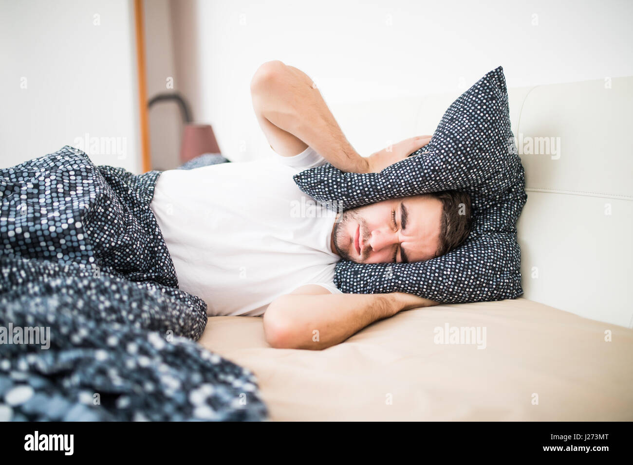 Too noisy to sleep. Handsome man covering his head and ears blocking