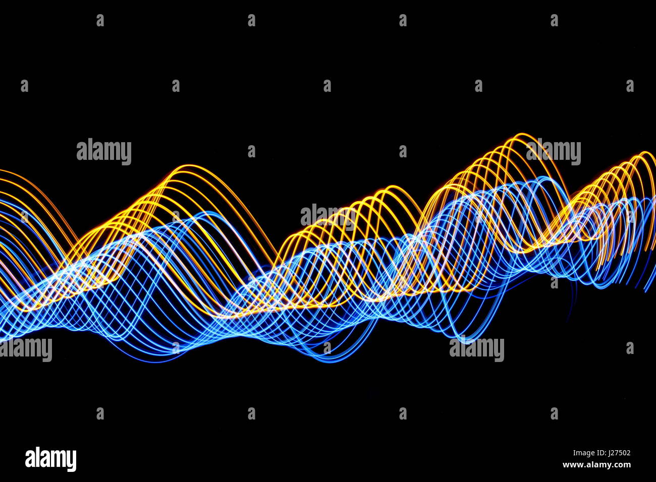 Long exposure photograph of neon blue and gold colour in an abstract wavy pattern against a black background. Light painting photography. Stock Photo